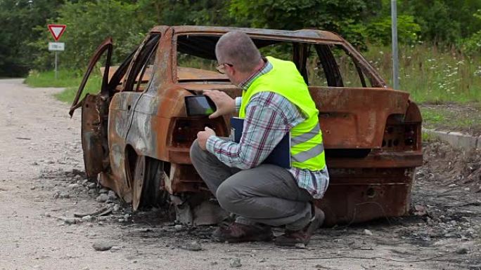 检查员使用平板电脑在路边烧毁的汽车残骸附近