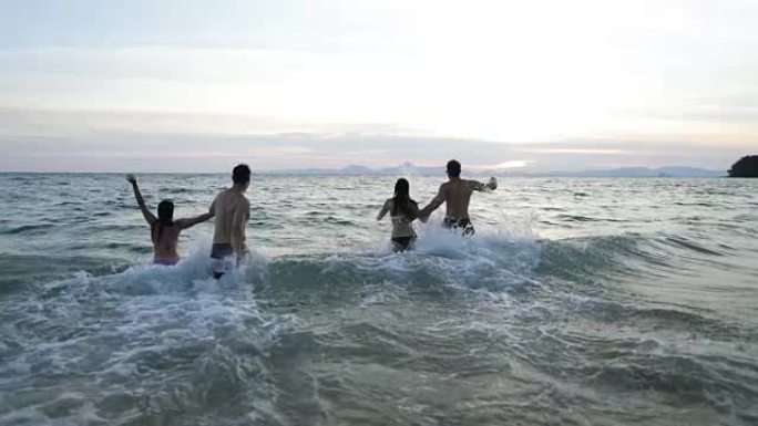 两对情侣在海水中奔跑，手牵着手，一群朋友在日落时在海滩上玩得开心