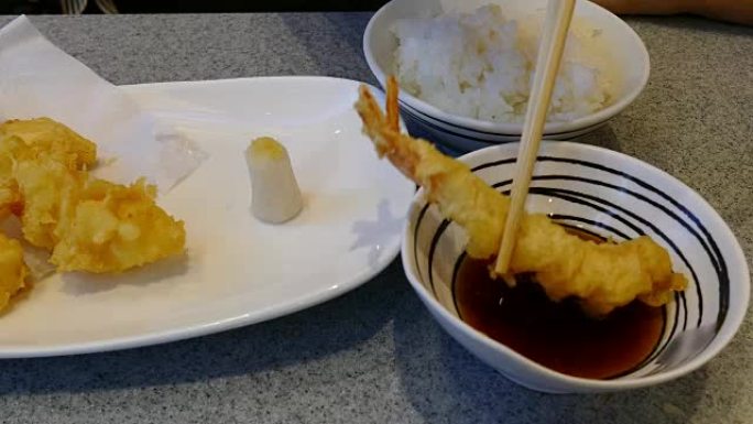 女人的手用筷子吃油炸虾虾-天妇罗日本食物