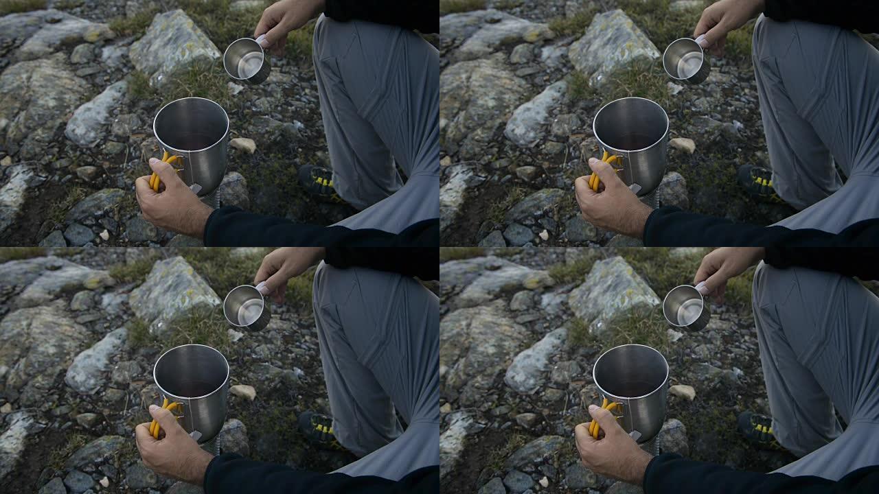 夏季户外日出时，年轻的成年男子在篝火旁山湖附近喝茶