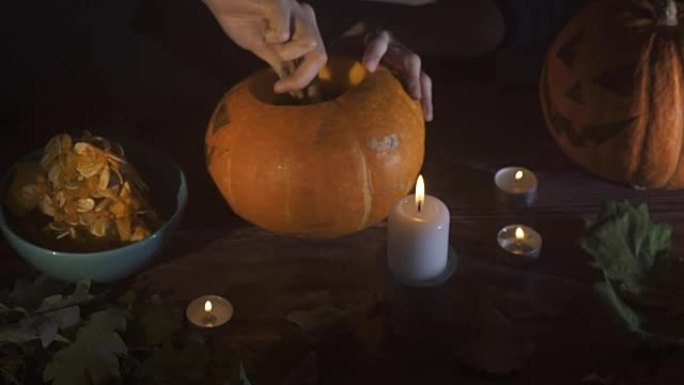 女性的手在晚上用蜡烛在木桌上sc出南瓜的种子和内容物。万圣节主题，杰克灯