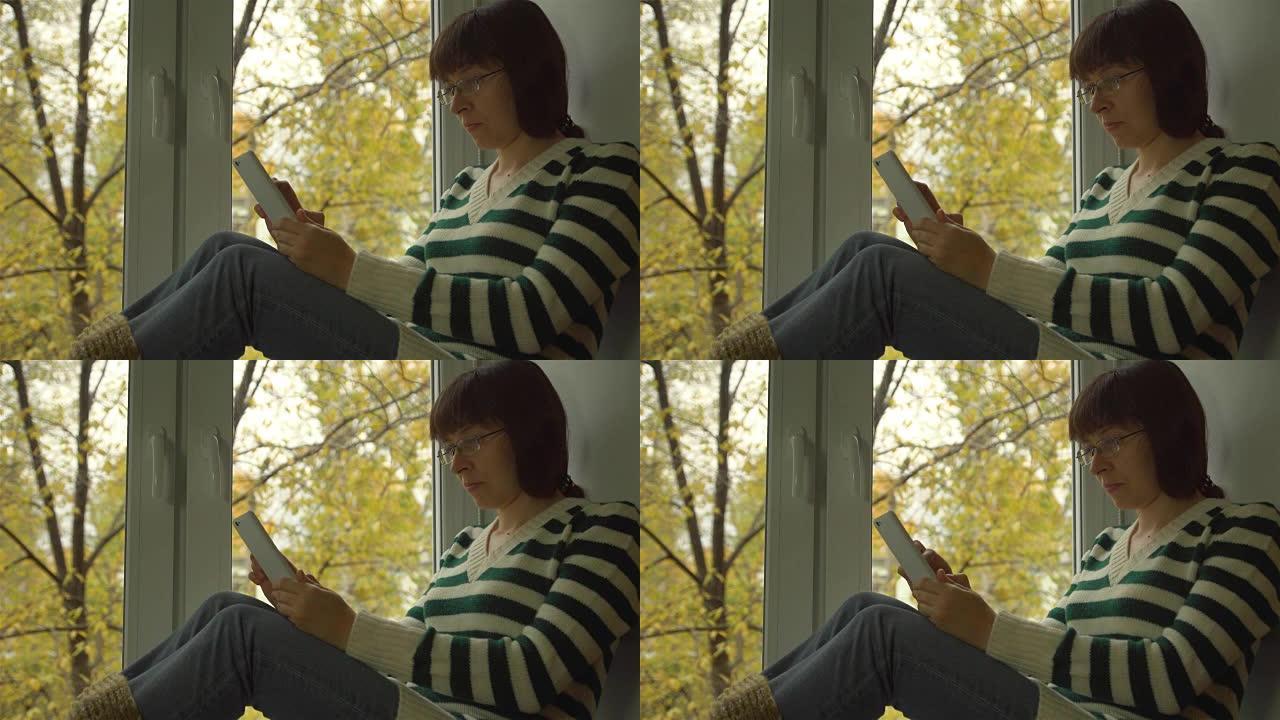 女孩坐在街上的窗台上黄叶，在网上看书。