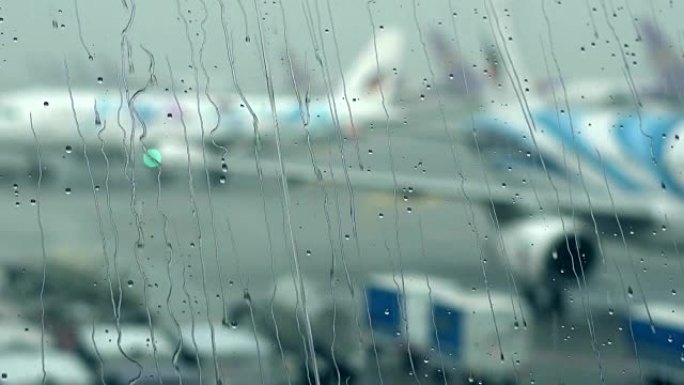机场航站楼窗户上的雨滴，外面模糊机场。慢动作