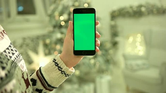 手机上女性双手触摸绿屏的特写。色度键。特写。跟踪运动。垂直。带有模糊的圣诞装饰背景