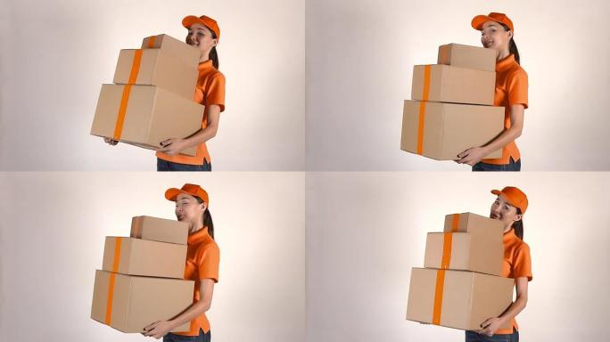 穿着橙色快递制服的漂亮女孩送一叠纸箱。浅灰色背景，全高清工作室拍摄