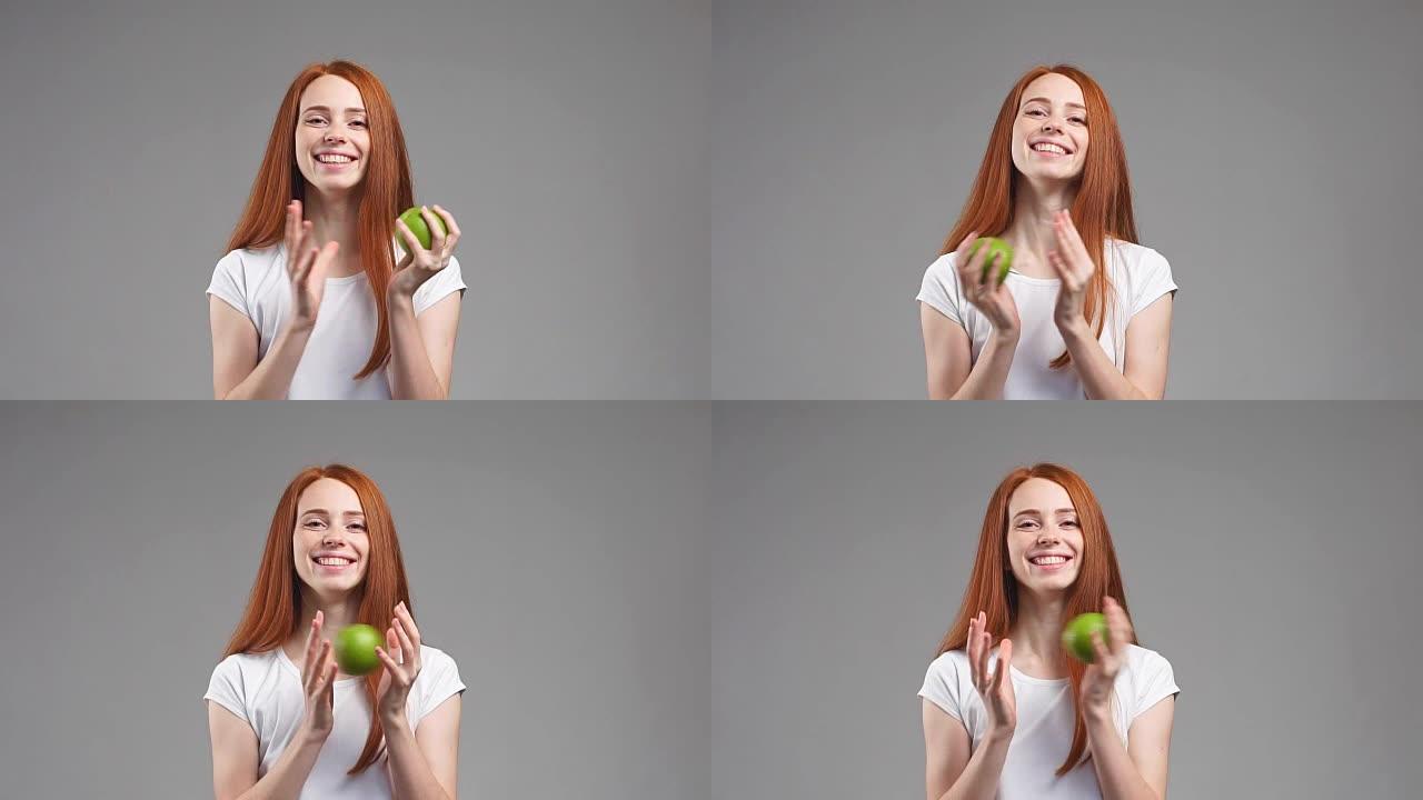 美丽的红发女孩，手里拿着一个绿色的苹果，在白色背景上微笑。慢动作