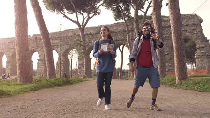 年轻夫妇背包客游客在罗马公园的罗马渡槽拱门附近散步，日出时带着吉他和睡袋慢动作steadycam