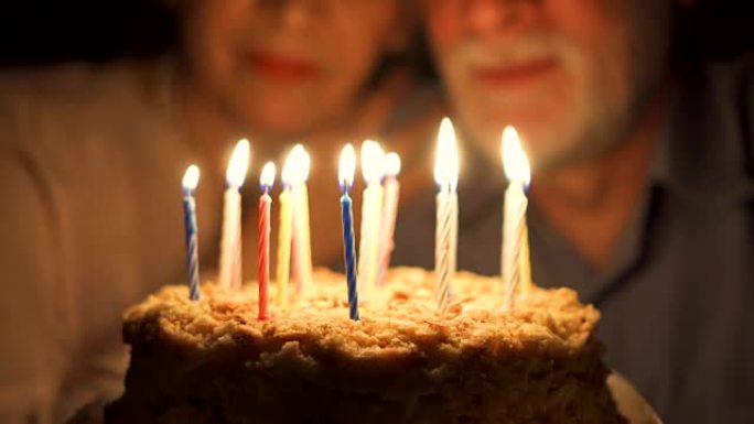 充满爱心的高级夫妇晚上在家用蛋糕庆祝周年纪念日。吹灭蜡烛