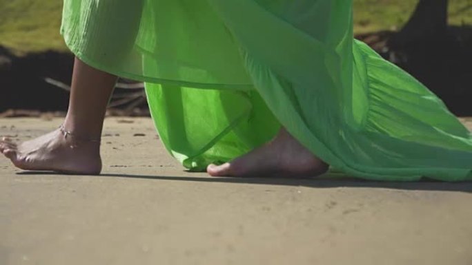 一个穿着绿色连衣裙沿着沙子行走的女孩的腿。