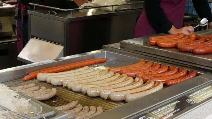 一个女推销员在烤架上烤香肠，布拉格市中心的街头食品，街道托盘柜台上的各种不同香肠
