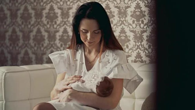 年轻的母亲双手抱着可爱的新生婴儿。室内特写镜头。