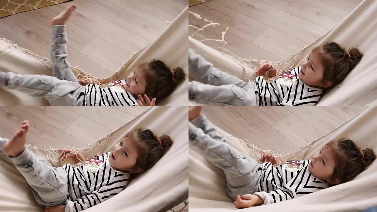 快乐的小女孩在室内玩得开心，躺在吊床上，挥舞着双腿。微笑的孩子