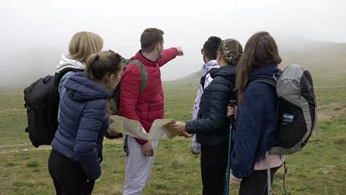 专业导游人员用背包向年轻游客解释路线阅读纸质地图并在山上带领路线
