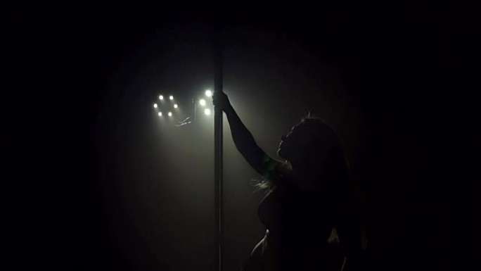 一个性感的舞者在黑暗中靠近一根钢管的肖像。