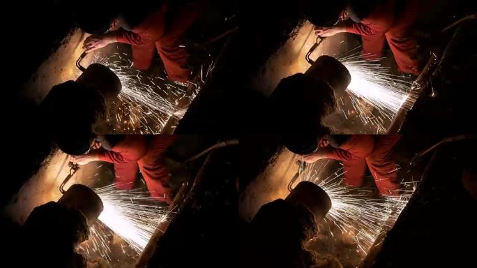 晚上进行高角度射击，一名工人精细切割破裂的管道，以便将其与新管道焊接在一起