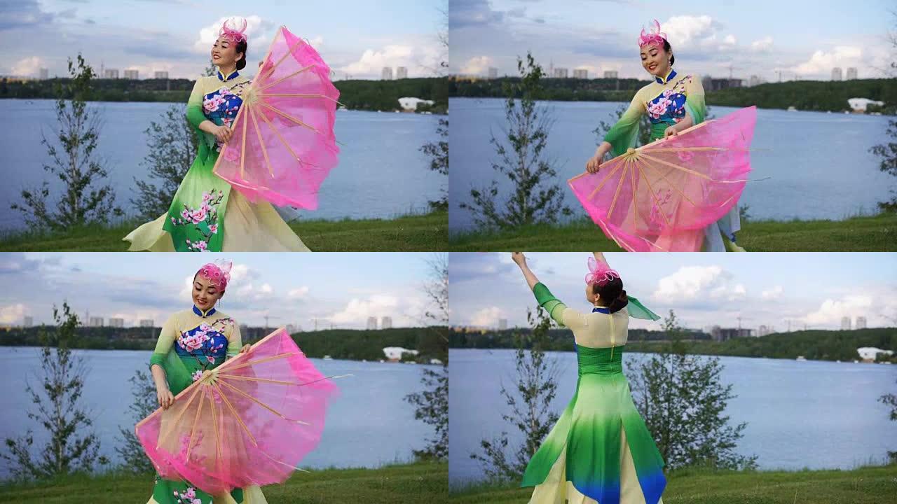 穿着中国传统服装的美丽中国女孩在河岸上与粉红色的大风扇跳舞