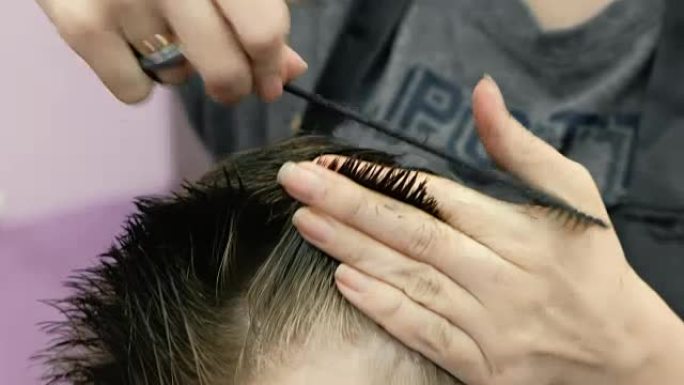 特写理发师的手用剪刀梳理和剪掉金色短男孩的头发。前视图。