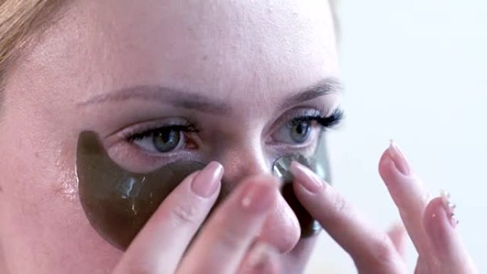 女人在眼睛下面贴了一个清爽的保湿面膜。白色背景的浴室内部有胶原蛋白垫的女性。