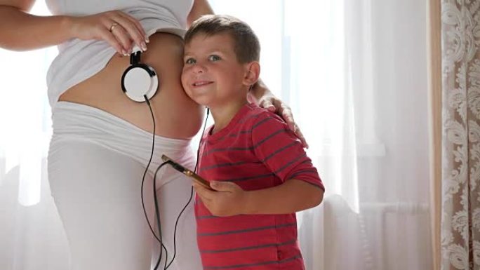 孩子把耳机放在孕妇的肚子上，肚子里的婴儿在家听音乐
