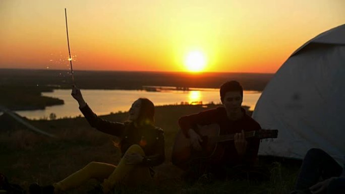 开朗的年轻朋友一起玩乐，在山上日落时弹吉他