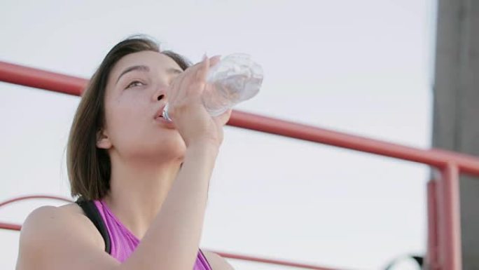 年轻健康的运动员从坐在体育场领奖台上的瓶子里喝水