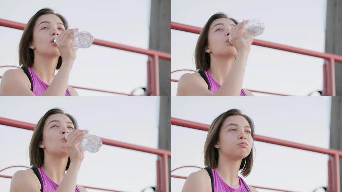年轻健康的运动员从坐在体育场领奖台上的瓶子里喝水