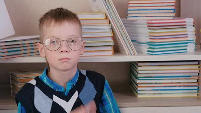 疲倦的七岁男孩戴着眼镜坐在书本中的地板上。