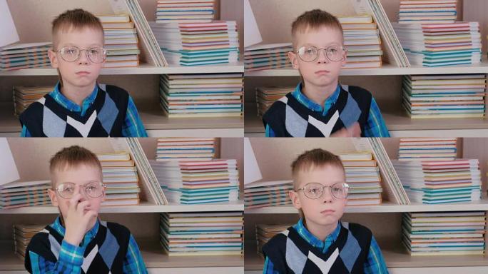 疲倦的七岁男孩戴着眼镜坐在书本中的地板上。