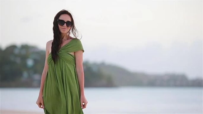 热带海滨的年轻美女。海滩上绿色德里斯的旅游女孩