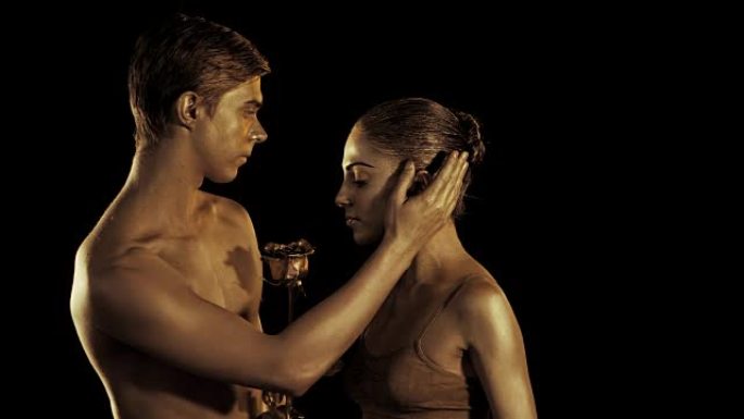 专业芭蕾舞演员在黑烟场景中由性伴侣与金色人体艺术表演。闪亮的金色皮肤。爱上女孩的男人呈现她的玫瑰花。