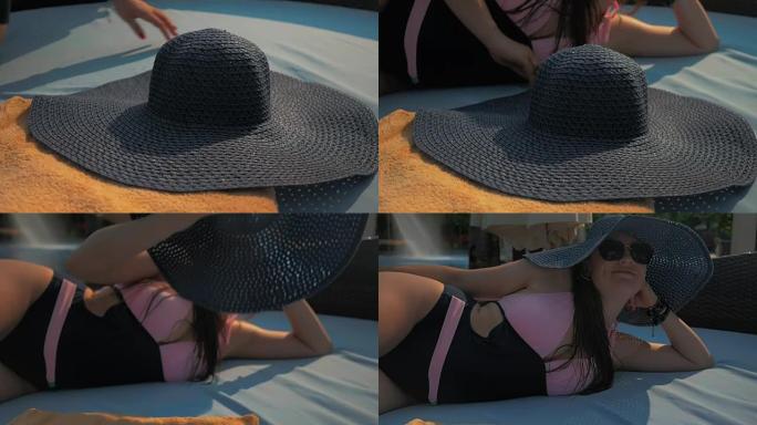 美丽的女孩正戴上蓝色的帽子，躺在躺椅上。夏日的阳光。慢动作。