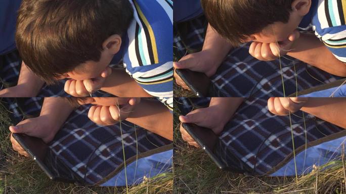 小男孩的特写镜头躺在大自然的地毯上，手里拿着手机
