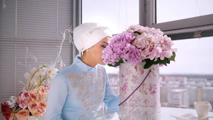 美丽的穆斯林新娘，穿着蓝色传统服装，为坐在窗边的尼卡化妆