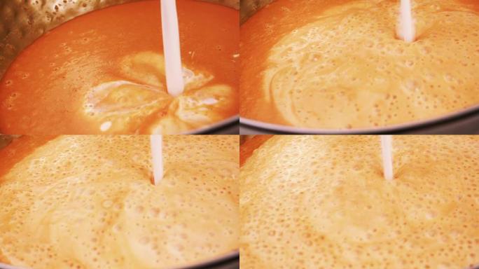 从一碗橙色焦糖糖浆中倒出细流牛奶。慢动作。