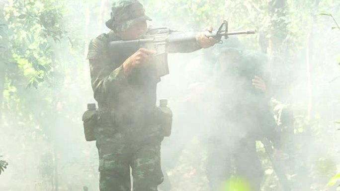 手持枪械的士兵穿着带烟雾的装甲制服。士兵们正把受伤的人抬出丛林。