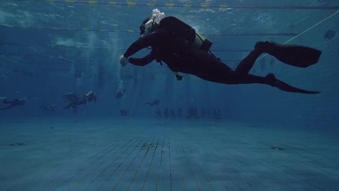 戴水肺的潜水员在游泳池的水下漂浮。学习水肺潜水课程