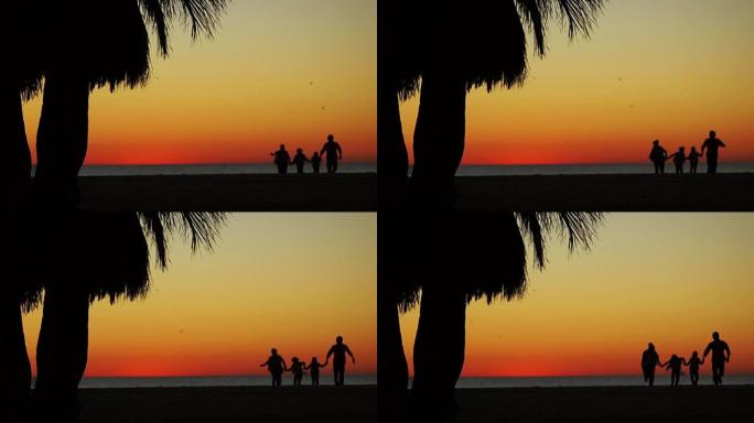 一个幸福的家庭沿着海滩奔跑。深色剪影，在日落鸟儿飞翔的背景下
