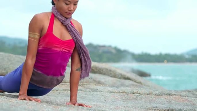 女人瑜伽练习致敬太阳，狗姿势，眼镜蛇姿势在海滩上