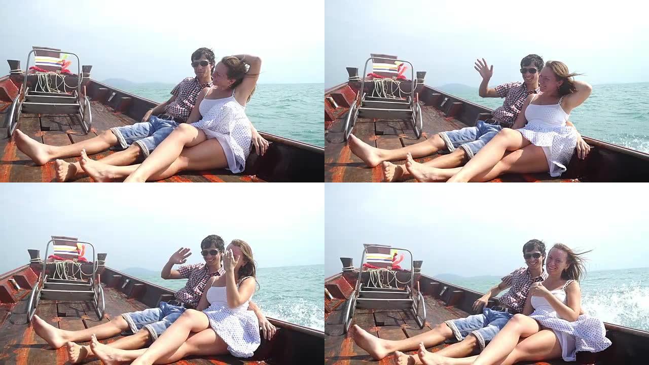 年轻幸福的夫妇坐在漂流木船的甲板上享受假期。向摄像机挥舞手臂。慢动作，1920x1080