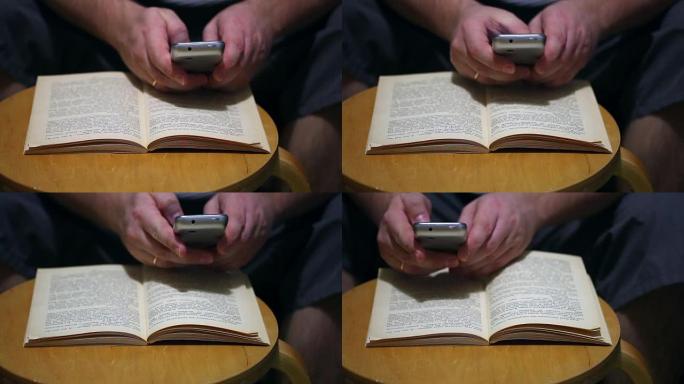 一名男子在纸质书的智能手机页面上拍照。打开的书放在椅子上。