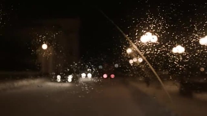 司机在城市的雨夜开车，从里面看。镜头。雨中汽车挡风玻璃上的景色