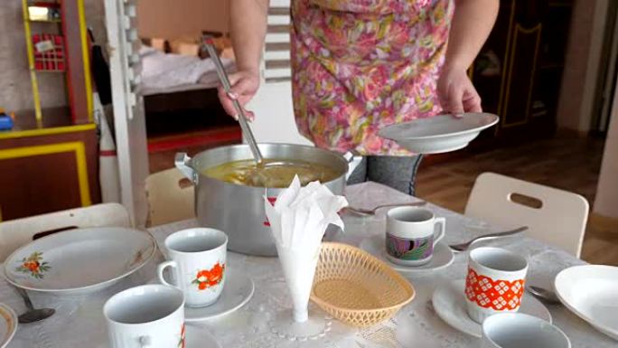 一锅汤和一个空盘子和一个勺子的手。肉汤、器皿和厨房用具制成的钢制平底锅。在市政机构中分配食物