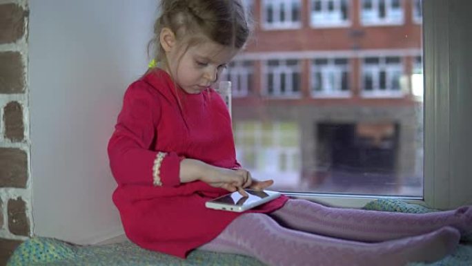 一个穿着粉色裙子的可爱小女孩坐在窗台上用智能手机