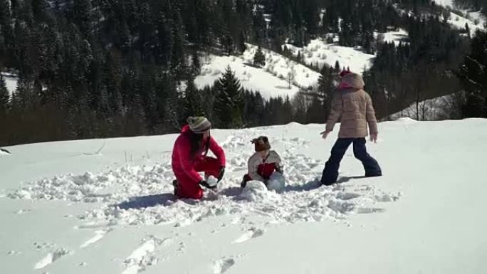 快乐的家庭在冬天在山上的白雪皑皑的森林里玩耍。妈妈和她的两个孩子扔雪球。他们在笑。
