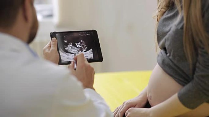 医生向孕妇展示了平板电脑上的超声波照片。一位幸福的未来母亲欣赏她的婴儿超声波的照片。