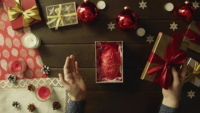 成年男子在装饰的木桌上打开带有真正人类心脏的圣诞礼品盒，顶部向下拍摄