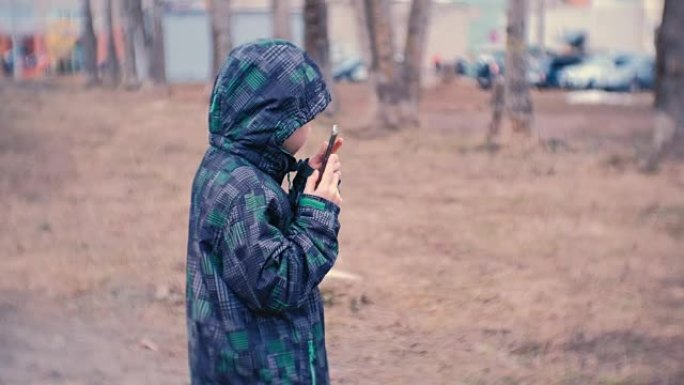 男孩在公园里拨打一个号码，用手机说话。