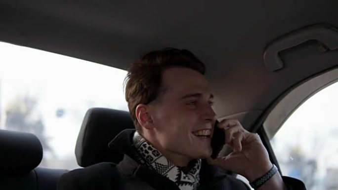 迷人的性感的家伙在黑色时髦的外套是微笑，而与某人在电话在汽车里。