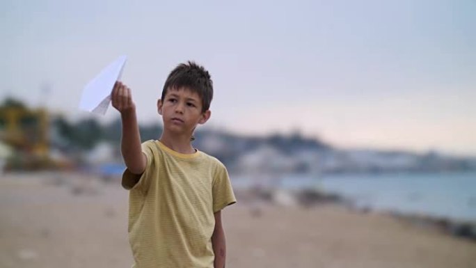 热情的男孩晚上在海边玩纸飞机