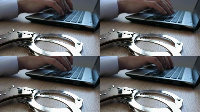 男子在笔记本电脑上工作，手铐在桌子上。在线网络犯罪概念。